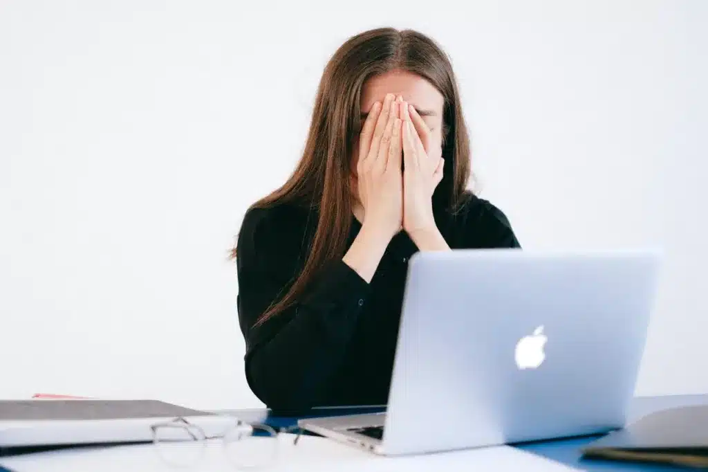 stress symptomer - kvinde begraver ansigtet i hænderne foran MacBook computer